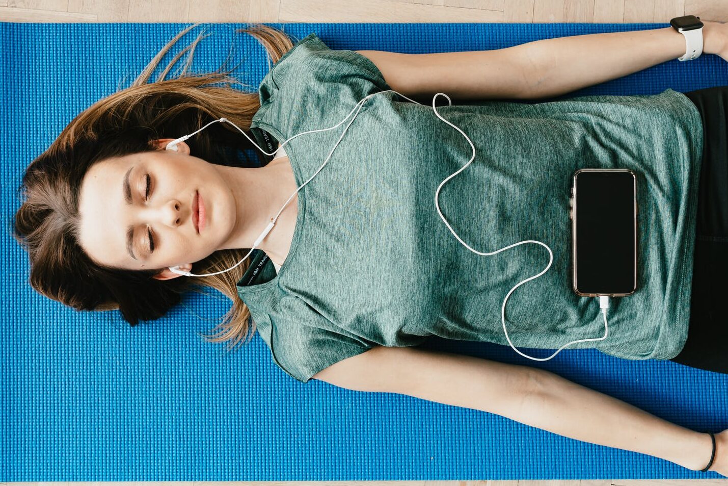 peaceful woman in earphones resting in shavasana pose at home