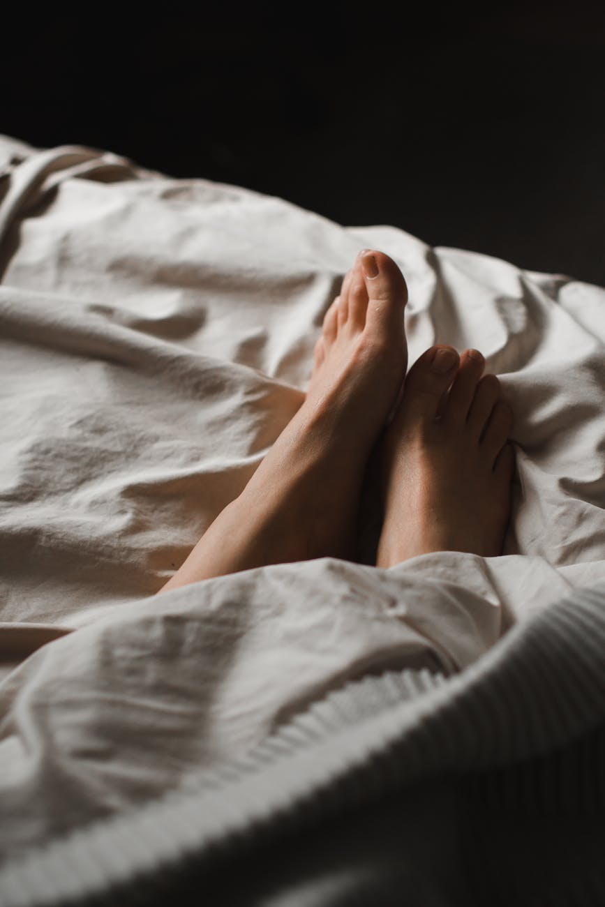 crop unrecognizable female feet lying in cozy bed